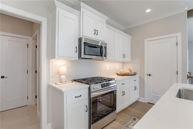 kitchen featuring tasteful backsplash, white cabinets, ornamental molding, stainless steel appliances, and light hardwood / wood-style flooring