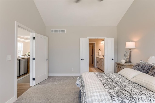 bedroom featuring vaulted ceiling, light colored carpet, and ensuite bathroom