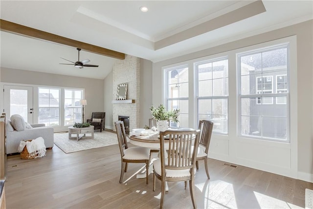 dining room featuring a raised ceiling, a stone fireplace, hardwood / wood-style flooring, and lofted ceiling with beams