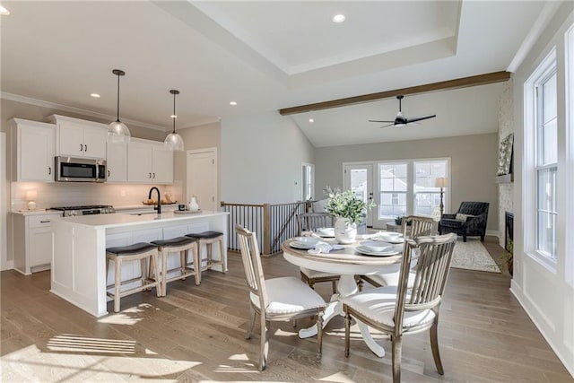 dining space with lofted ceiling with beams, crown molding, a large fireplace, and light hardwood / wood-style flooring