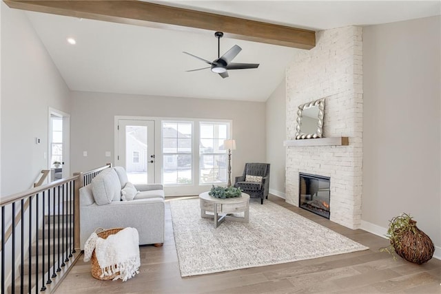 living room featuring a stone fireplace, hardwood / wood-style floors, high vaulted ceiling, ceiling fan, and beam ceiling