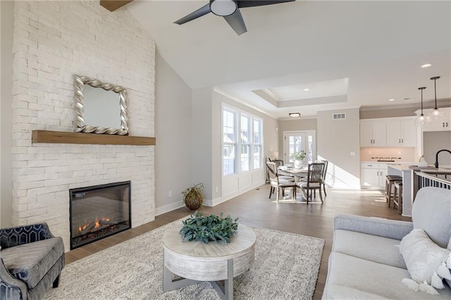 living room with sink, vaulted ceiling, light hardwood / wood-style flooring, a raised ceiling, and a fireplace