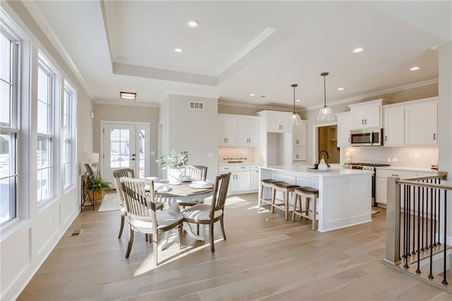 dining area with crown molding, a tray ceiling, sink, and light wood-type flooring