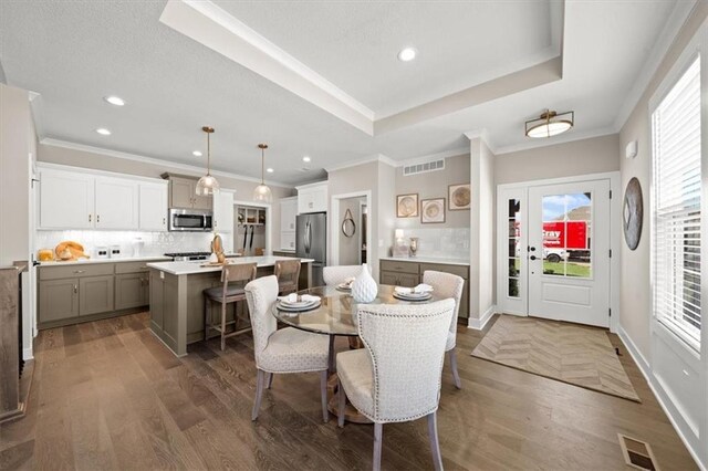 dining room with dark hardwood / wood-style flooring, a raised ceiling, and ornamental molding