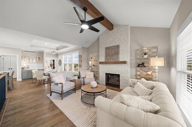 living room with dark hardwood / wood-style floors, ceiling fan, a stone fireplace, and lofted ceiling with beams