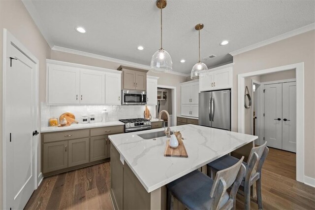 kitchen featuring sink, hanging light fixtures, stainless steel appliances, tasteful backsplash, and a kitchen island with sink