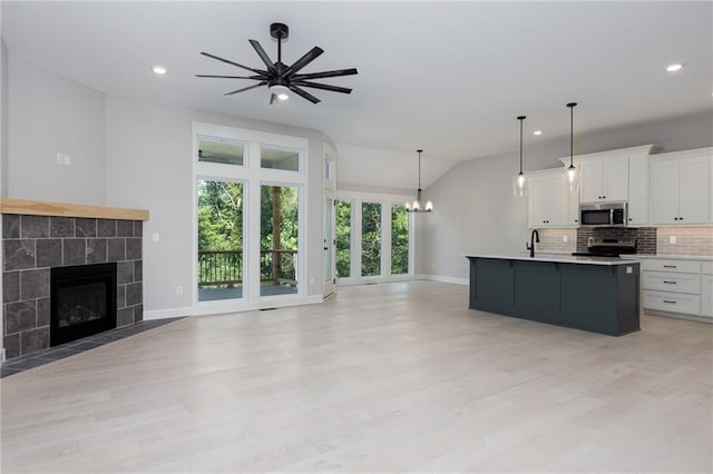 kitchen with stainless steel appliances, ceiling fan with notable chandelier, a center island with sink, white cabinetry, and light hardwood / wood-style floors