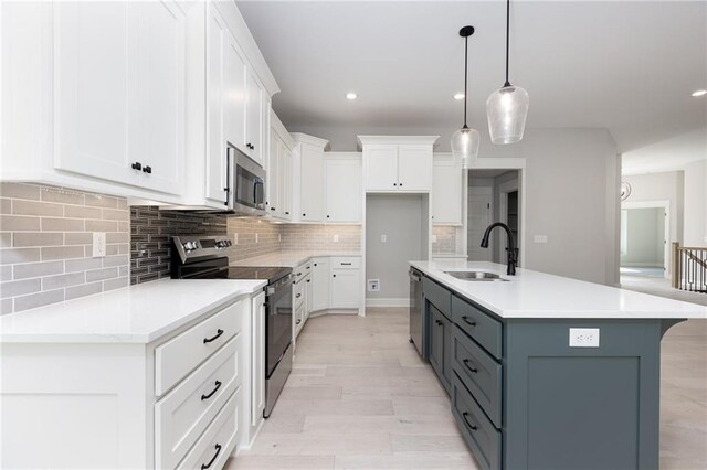 kitchen featuring appliances with stainless steel finishes, backsplash, a center island with sink, and white cabinets