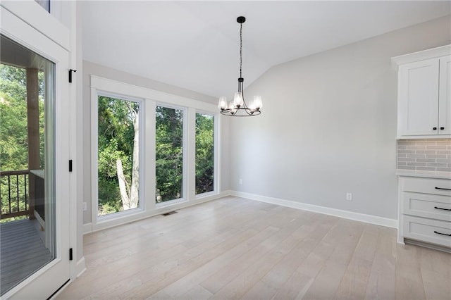 unfurnished dining area with an inviting chandelier, vaulted ceiling, and light hardwood / wood-style floors