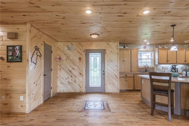 kitchen with wooden walls, light brown cabinetry, pendant lighting, and sink