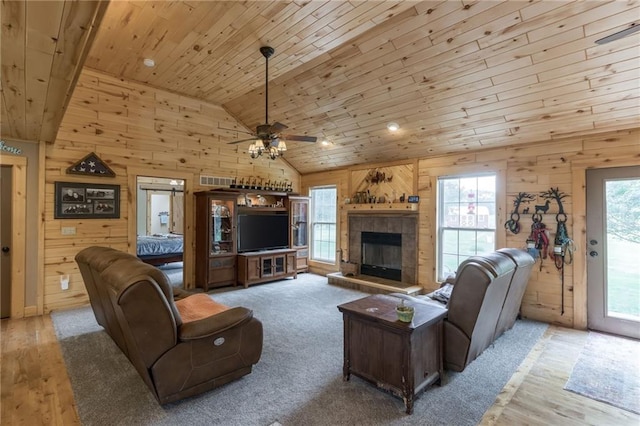 carpeted living room with ceiling fan, a stone fireplace, wood ceiling, and wooden walls