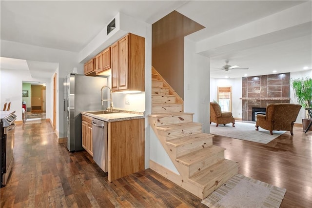 kitchen featuring sink, ceiling fan, stainless steel appliances, a fireplace, and dark hardwood / wood-style flooring