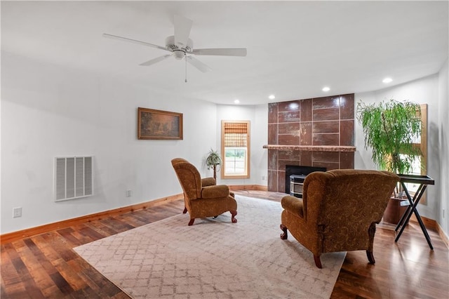 living room with ceiling fan, wood-type flooring, and a tile fireplace