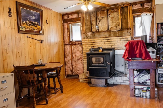 interior space featuring ceiling fan, a wood stove, wooden walls, and light wood-type flooring