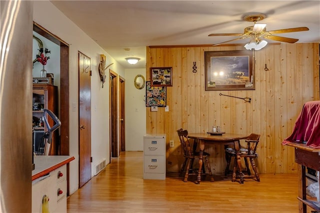 dining space featuring ceiling fan, wooden walls, and light wood-type flooring