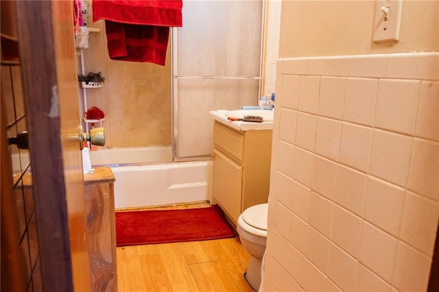 full bathroom featuring combined bath / shower with glass door, wood-type flooring, tile walls, vanity, and toilet