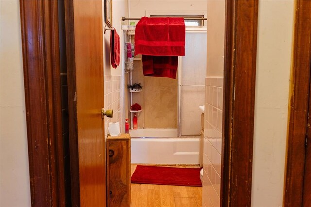 bathroom featuring tile walls, hardwood / wood-style floors, and bath / shower combo with glass door