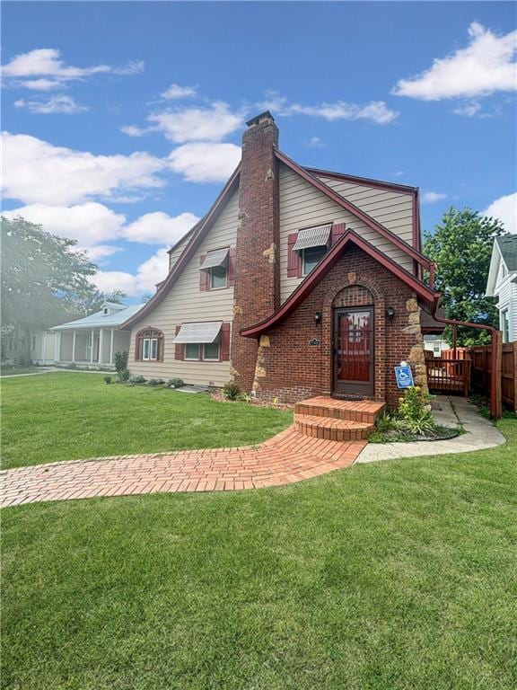 rear view of house with a chimney, fence, a lawn, and brick siding