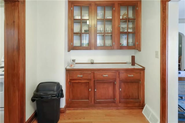 bar featuring light wood finished floors, baseboards, visible vents, and arched walkways