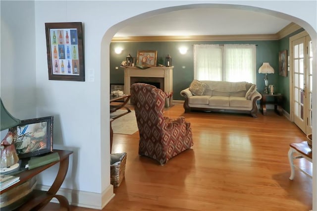 living area featuring arched walkways, ornamental molding, wood finished floors, and baseboards