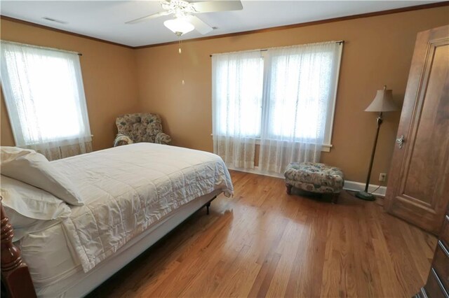 bedroom with multiple windows, hardwood / wood-style flooring, crown molding, and ceiling fan