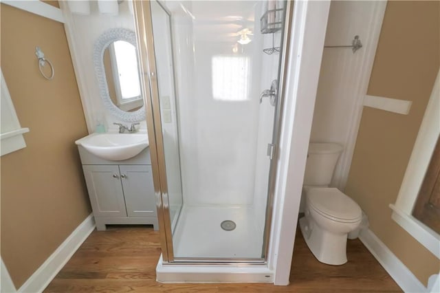 full bath with toilet, wood finished floors, vanity, baseboards, and a stall shower