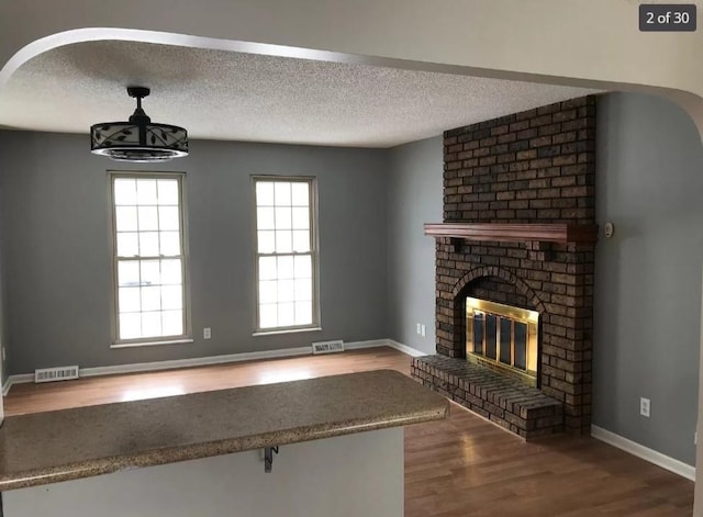 unfurnished living room featuring hardwood / wood-style floors, a textured ceiling, and a brick fireplace