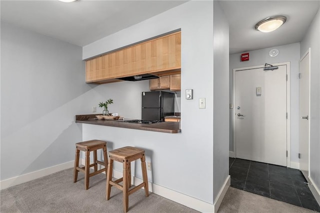 kitchen featuring dark colored carpet, a kitchen breakfast bar, black refrigerator, and kitchen peninsula