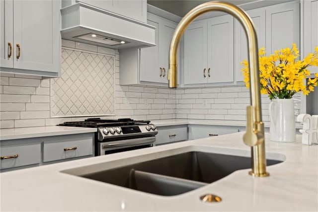 kitchen with custom exhaust hood, gray cabinets, tasteful backsplash, and gas range