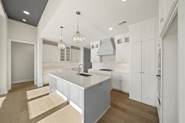 kitchen featuring a center island with sink, white cabinetry, and custom range hood