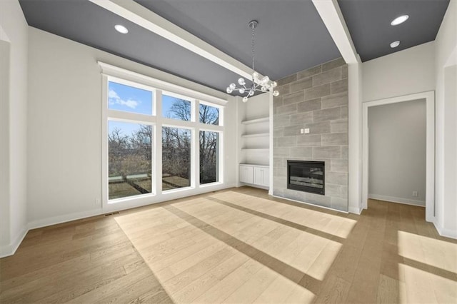 unfurnished living room with a chandelier, built in shelves, a tiled fireplace, and wood-type flooring