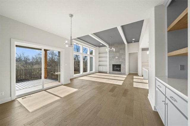 unfurnished living room featuring a tile fireplace, built in features, beamed ceiling, a notable chandelier, and wood-type flooring