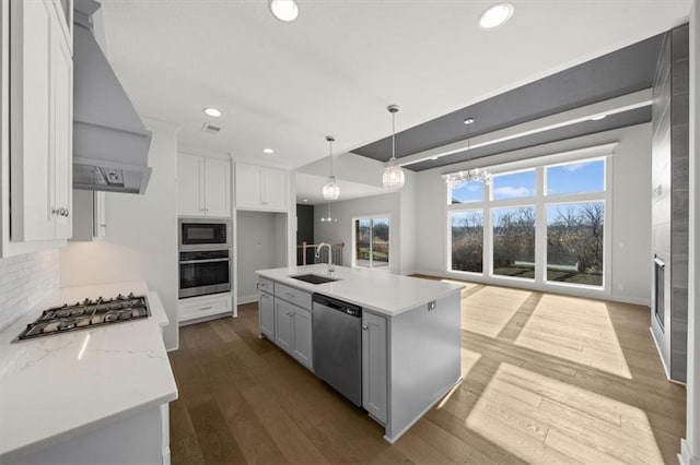 kitchen with stainless steel appliances, wall chimney range hood, sink, a center island with sink, and white cabinets