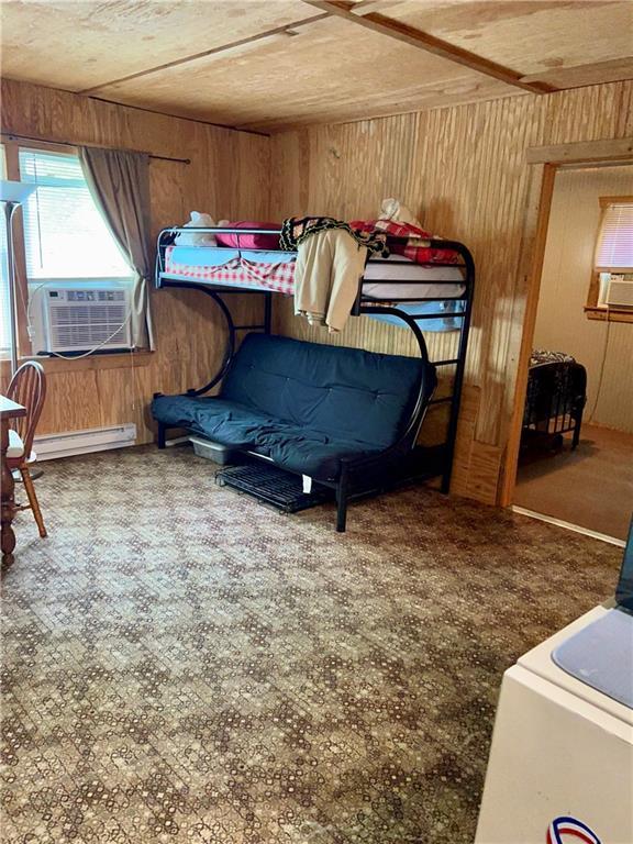 bedroom with wood walls, a baseboard radiator, and cooling unit