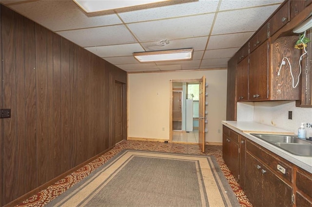 kitchen with sink, a paneled ceiling, dark brown cabinetry, and wood walls