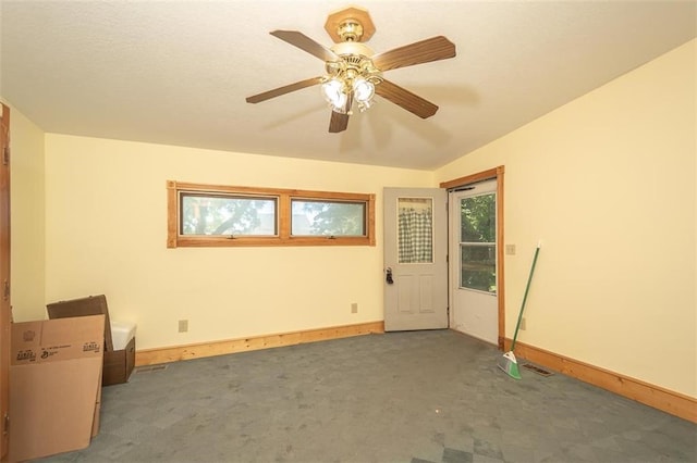 empty room featuring a wealth of natural light, ceiling fan, and dark carpet