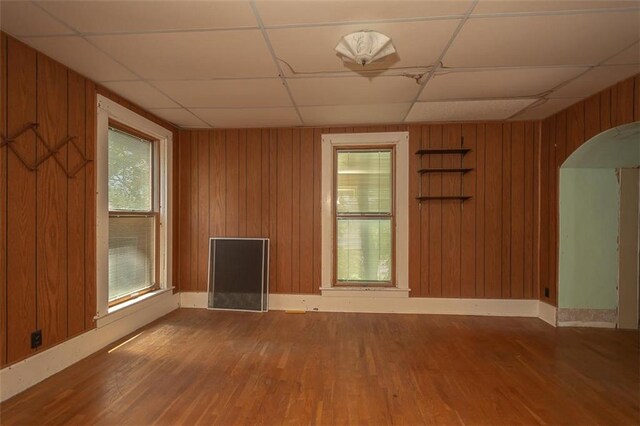 empty room featuring a drop ceiling, wood walls, and wood-type flooring