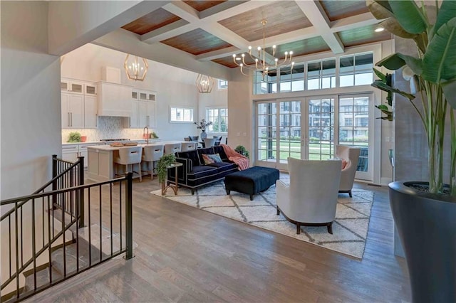 living room with beam ceiling, a notable chandelier, hardwood / wood-style floors, and coffered ceiling