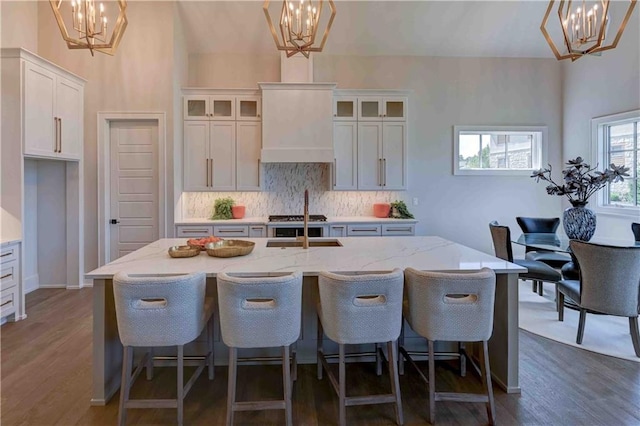 kitchen with dark wood-type flooring, hanging light fixtures, white cabinets, and a center island with sink