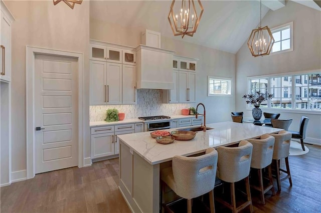 kitchen with wood-type flooring, a kitchen island with sink, sink, and high vaulted ceiling