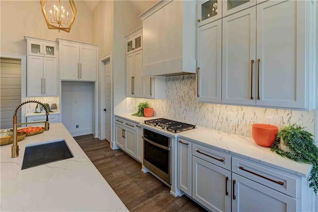 kitchen featuring dark wood-type flooring, light stone counters, custom exhaust hood, appliances with stainless steel finishes, and pendant lighting