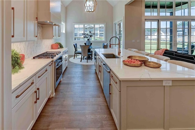 kitchen featuring a center island with sink, wall chimney range hood, sink, light stone counters, and hardwood / wood-style flooring