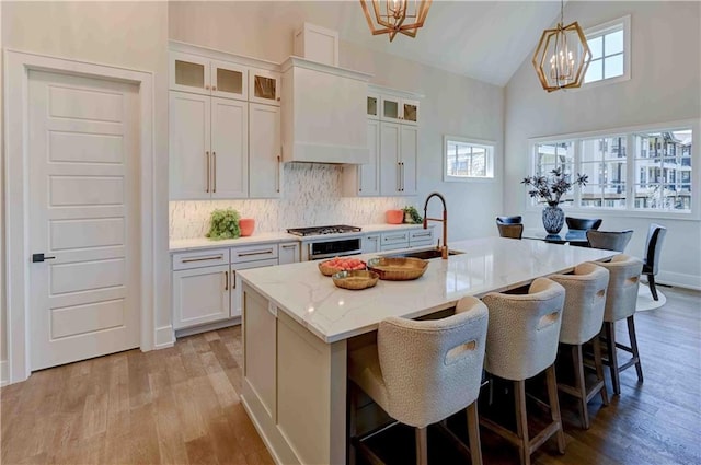 kitchen with light hardwood / wood-style flooring, a chandelier, an island with sink, hanging light fixtures, and a healthy amount of sunlight