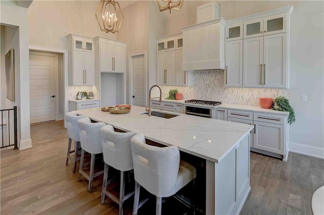 kitchen featuring backsplash, wood-type flooring, a center island with sink, and a towering ceiling