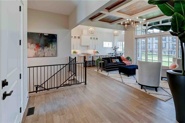 hall featuring beam ceiling, a notable chandelier, coffered ceiling, and light wood-type flooring