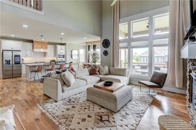 living room with a fireplace, light wood-type flooring, and a high ceiling