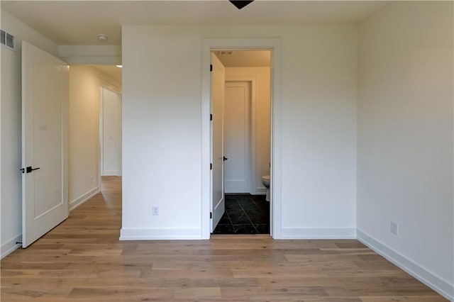 unfurnished bedroom with ensuite bathroom and light hardwood / wood-style flooring