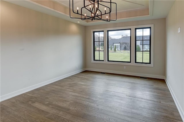 unfurnished dining area featuring a chandelier, hardwood / wood-style flooring, and a tray ceiling