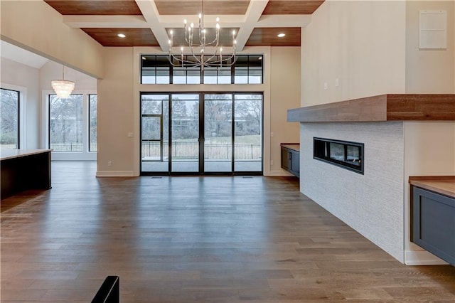 unfurnished living room with beam ceiling, dark hardwood / wood-style flooring, a chandelier, and coffered ceiling