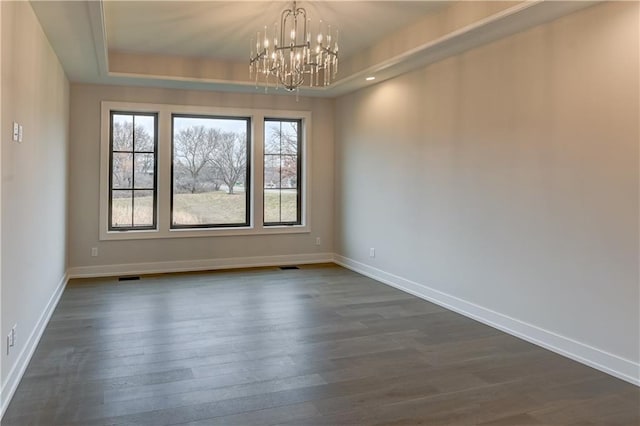 spare room featuring a raised ceiling, dark wood-type flooring, and a chandelier